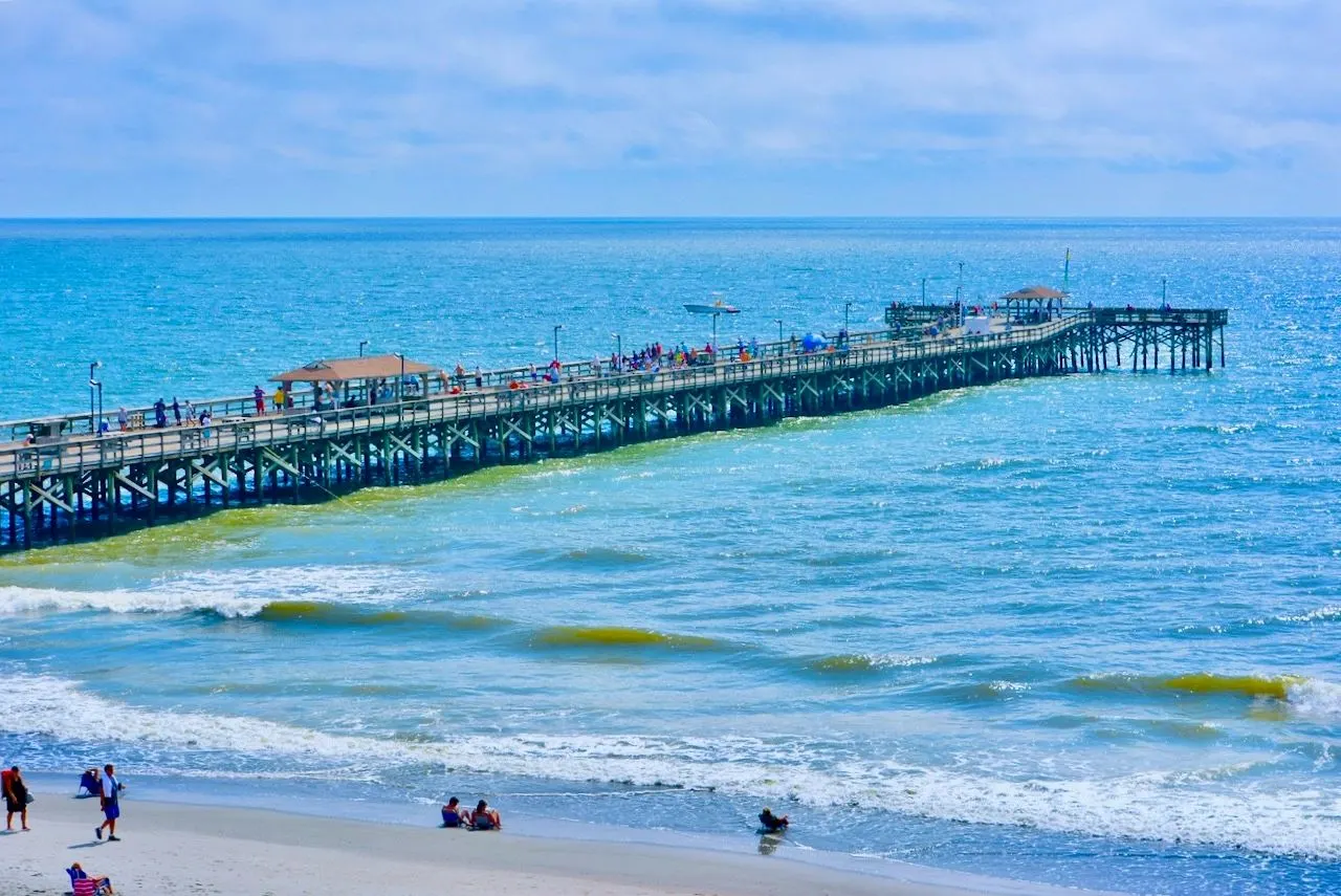 Long pier stretching into the ocean, with people on the beach below