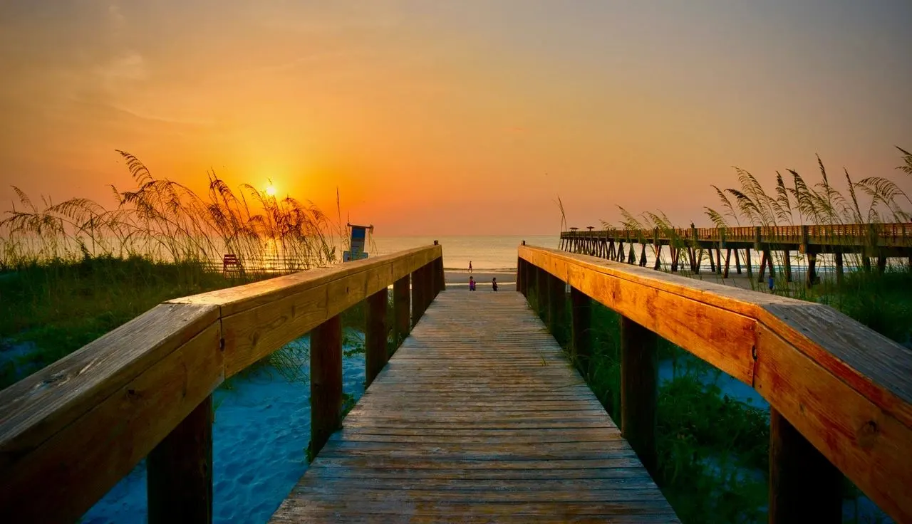 Boardwalk through the sea oats toward the sun rising over the ocean