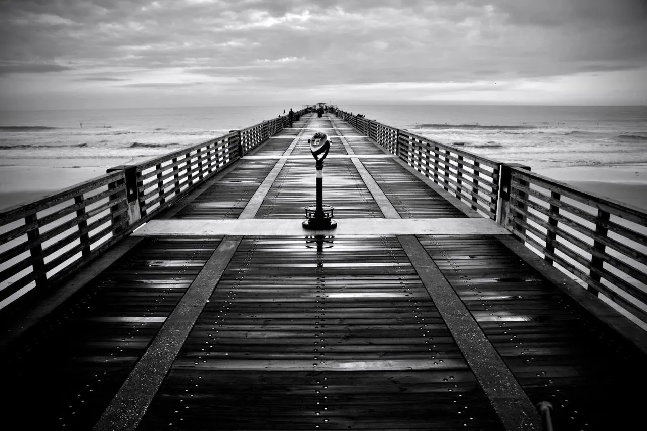 Black-and-white view down a long wooden pier